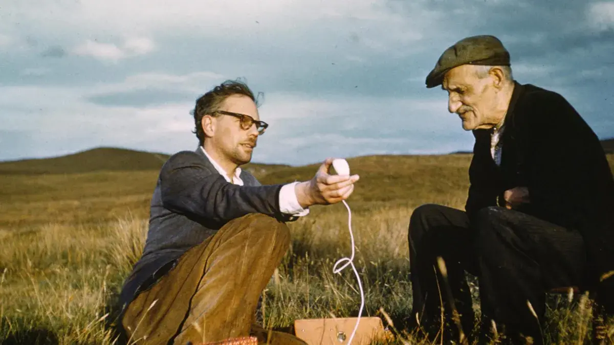 Researcher interviewing Gaelic storyteller in a field. 