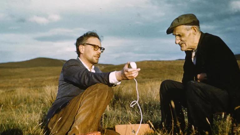 Researcher interviewing Gaelic storyteller in a field. 